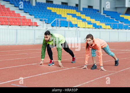 Determined athletes, man and woman, starting race on running track in empty stadium Stock Photo