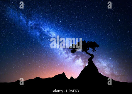 Starry sky with blue Milky Way. Night landscape with alone tree on the mountain peak against colorful milky way. Amazing galaxy. Nature background Stock Photo