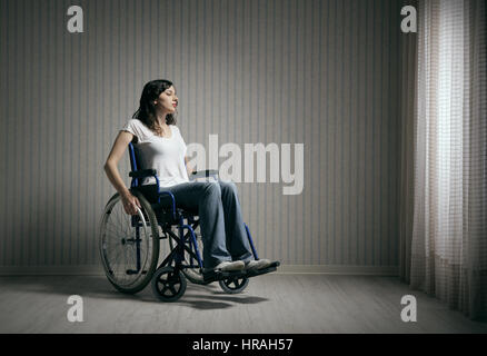 Sad woman sitting on wheelchair in empty room Stock Photo