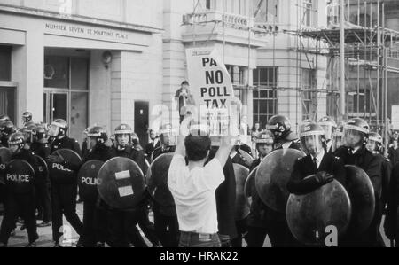 A protestor holds up a placard to a line of riot police during the Poll Tax Riots in London, England on March 31, 1990. The unpopular tax was introduced by the Conservative government led by Prime Minister Margaret Thatcher. Stock Photo
