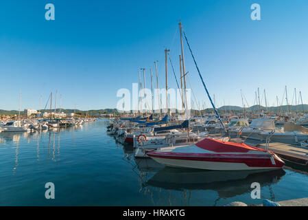 Ibiza sunshine in Late afternoon in St Antoni de Portmany, Ibiza, Spain.  Row of idle watercraft, sailboats & yachts.  Boat in foreground needs paint. Stock Photo