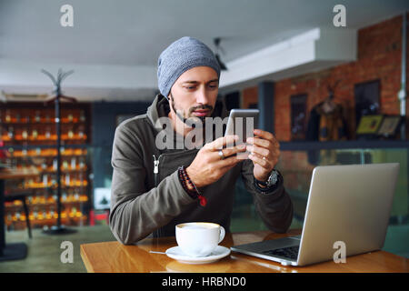 Cheerful hipster guy at the restaurant using a mobile phone. Stock Photo