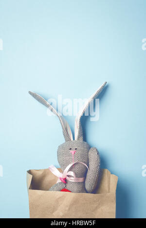 Easter bunny in a paper bag. Rabbit. Blue background. Easter ideas. Easter eggs. Space for text. Toned image. Trendy toning. Stock Photo