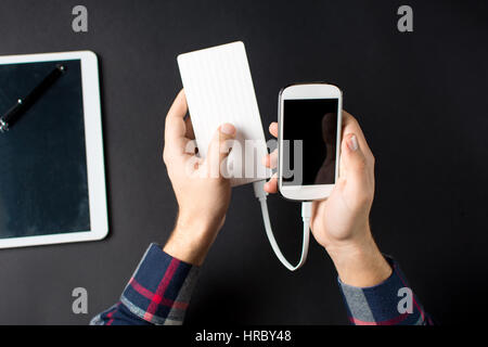 male hands holding a white cellphone connected to a power bank Stock Photo
