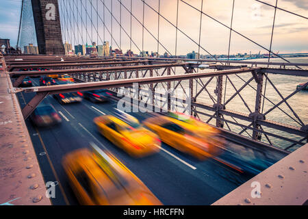 Yellow cab on Brooklyn Bridge in New York at cloudy sunset Stock Photo