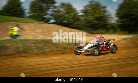 Red off-road buggy racing car on dry dirt track passing people on high speed Stock Photo