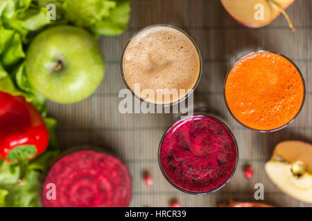 three glasses of different fresh juice. Beet, carrot and apple juices on grey wood background. Stock Photo