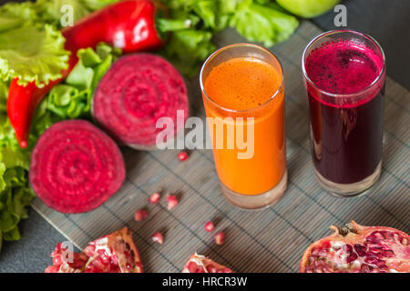 two glasses of different fresh juice. Beet and carrot juices on grey wood background. Stock Photo