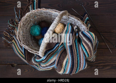 Knitted woolen scarf and yarn balls in a wicker basket on a wooden surface Stock Photo