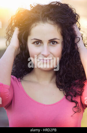 Charming young woman in pink shirt, lokks in to the camera, while picks her hair / Vintage style photo with a random white ballance, color effects. Stock Photo