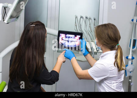 Healthy teeth. Female doctor dentist is showing x-ray teeth on tablet to young patient. Dentist or stomatologist is wearing medical clothing Stock Photo