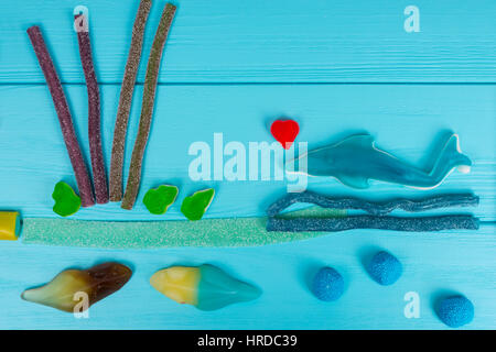 Cheerful picture of tasty jelly candies in the shape of fish and waves on wooden turquoise table Stock Photo