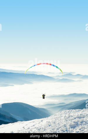 Paraglider flying in the sky over a snowy mountain top Stock Photo