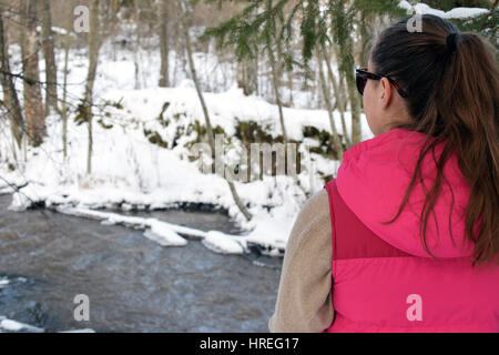 Young woman watching creek on winter forest. Stock Photo