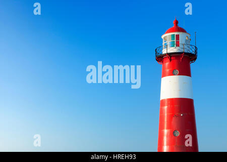 A red and white lighthouse at sea under a clear blue sky. Photographed near Westkapelle in Zeeland, The Netherlands. Stock Photo