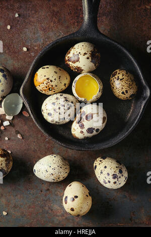 Whole and broken quail eggs with yolk in shell and pink sea salt crystal in small iron cast pan over old rusty texture metal background. Top view with Stock Photo