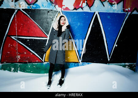 Pretty young woman in gray coat against graffiti wall in snow Stock Photo