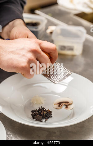 Chef rasping lemon zest over mushrooms, preparing his plate for soup Stock Photo
