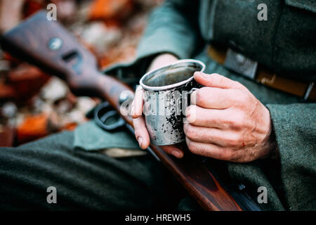 Unidentified Re-enactor Dressed As German Wehrmacht Infantry Soldier In World War II Holding Cup With Hot Water Or Tea In Camping In Autumn Forest. Stock Photo