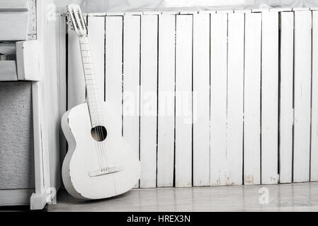 Old acoustic guitar leaning against the white wooden wall Stock Photo