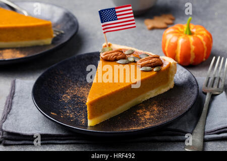 Pumpkin pie, tart made for Thanksgiving day on a black plate with American flag on top. Grey stone background. Stock Photo
