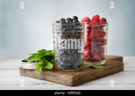 Raspberry and black currant in glass jars on wooden background Stock Photo