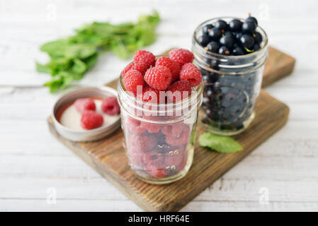 Raspberry and black currant in glass jars on wooden background Stock Photo