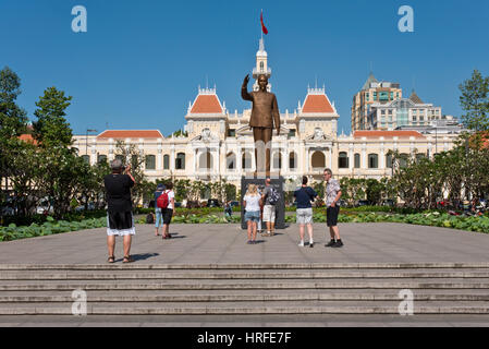 The bronze statue of Ho Chi Minh that stands outside the Ho Chi Minh City Hall on a sunny day with blue sky and tourists taking pictures. Stock Photo