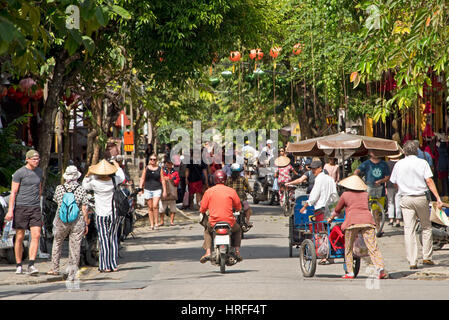 A compressed perspective street in Hoi An old town with tourists walking around, riding rickshaws and local people going about their daily business. Stock Photo