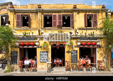 A street scene in Hoi An old town with tourists in a restaurant or cafe showing typical colonial architecture. Stock Photo