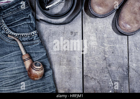Wooden pipe for smoking on blue jeans, gray wooden background with boots and empty space Stock Photo