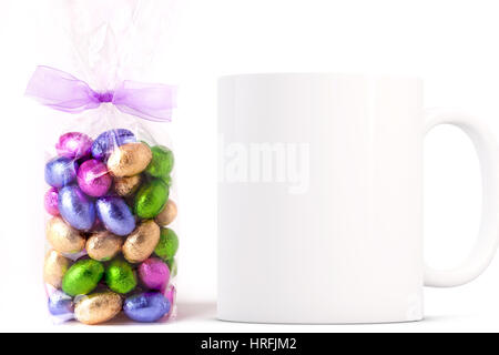 Easter coffee mug mockup next to a cellophane wrapped bag of gold wrapped chocolate mini eggs. Overlay your custom quotes and designs for selling mugs Stock Photo