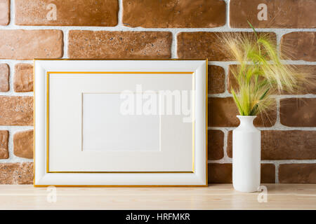 Gold decorated landscape frame mockup with ornamental grass in styled vase near exposed brick wall. Empty frame mock up for presentation design.  Temp Stock Photo