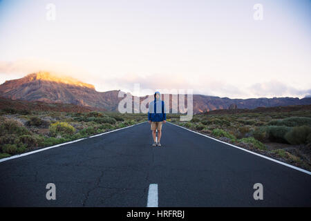 Portrait of man in blue jacket standing straight in the middle of road on mountains background, Tenerife Island Stock Photo