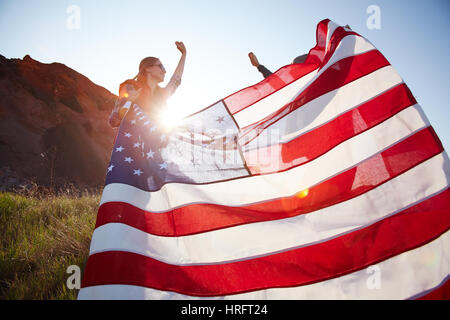 Young happy couple spreading big banner of America on top of hill taking hike in nature Stock Photo