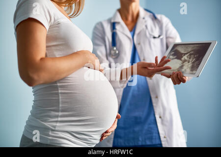 Mid-section image of unrecognizable female doctor explaining ultrasound scan results to pregnant woman using digital tablet Stock Photo