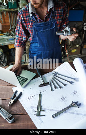 Unrecognizable modern mechanic working in garage at rough wooden table with assorted mechanics tools, wrenches, hammer and tongs, laid out on it with  Stock Photo