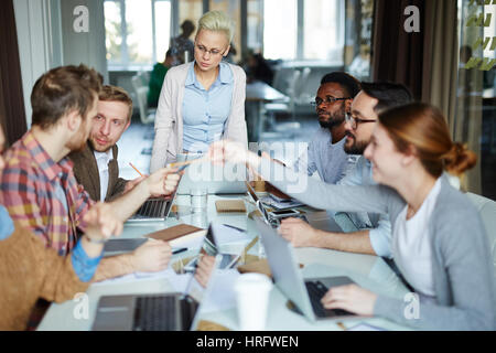 Enthusiastic male and female programmers creating new computer application while sitting in boardroom with glass wall Stock Photo