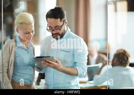 Waist-up portrait of male and female coworkers standing in meeting room and working on their business project with help of digital tablet Stock Photo