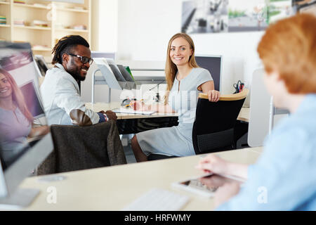 Creative group of interior designers sitting in modern office and listening to young red-haired colleague with interest Stock Photo