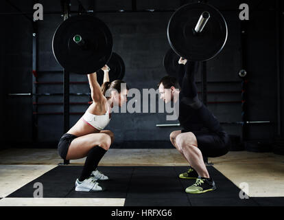 Motivational side view image of young man and woman performing overhead squats with huge heavy barbells looking at each other Stock Photo