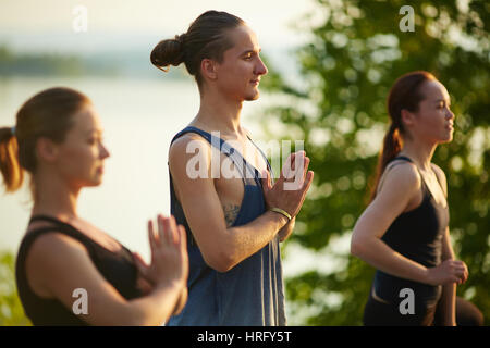 Close-up view of three friends holding hands in namaste while meditating outdoors Stock Photo