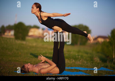 Young couple practicing front bird pose while doing acroyoga outdoors on summer evening Stock Photo