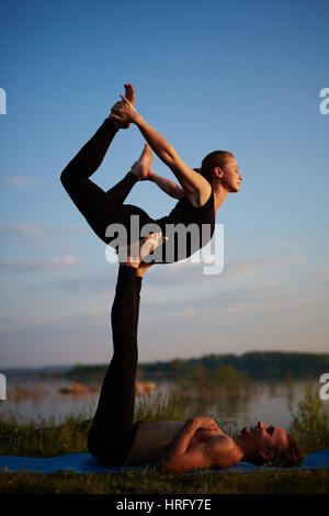 Experienced instructors balancing in front bird pose while doing acroyoga on late summer evening Stock Photo