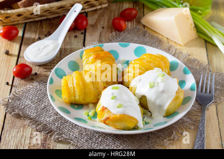 Baked potato with cheese served with cream sauce and greens on a wooden table in a rustic style. Stock Photo