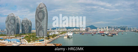 A 3 picture stitch panoramic view of Sanya Harbour with the Phoenix Island Resort left and fishing boats ships moored and the skyscrapers of the city. Stock Photo