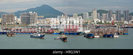 A 3 picture stitch panoramic view of Sanya harbour in China with fishing boats ships moored and the skyscrapers of the city behind. Stock Photo