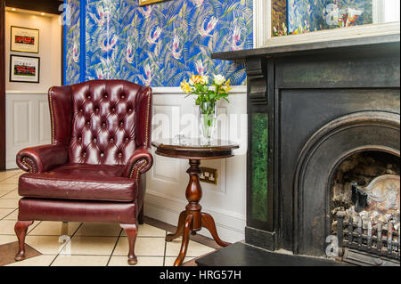 Gentleman's club style armchair next to a fireplace in a hotel reception. Stock Photo
