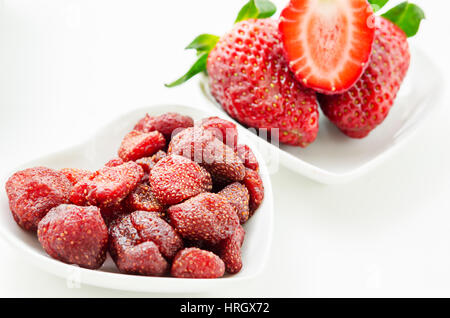 Dried strawberries in white bowl and fresh strawberry on white background. Stock Photo