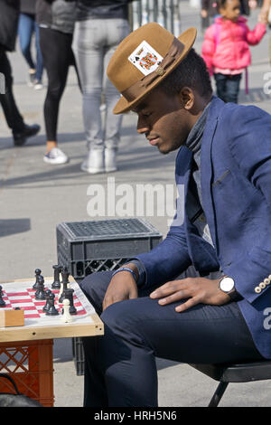 A nattily dressed man with an ace of spades card in his hat playing chess at Union Square Park in Manhattan, New York City. Stock Photo